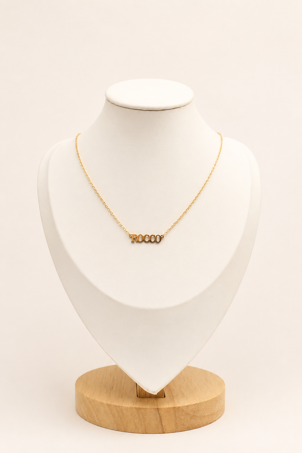Gold necklace on a white bust with a wooden base against a beige background