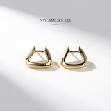 A pair of gold-toned geometric hoop earrings with a triangular open-frame design, displayed on a clean white surface with soft shadows. The brand name 'SYCAMORE LEE JEWELRY' is printed above the earrings.