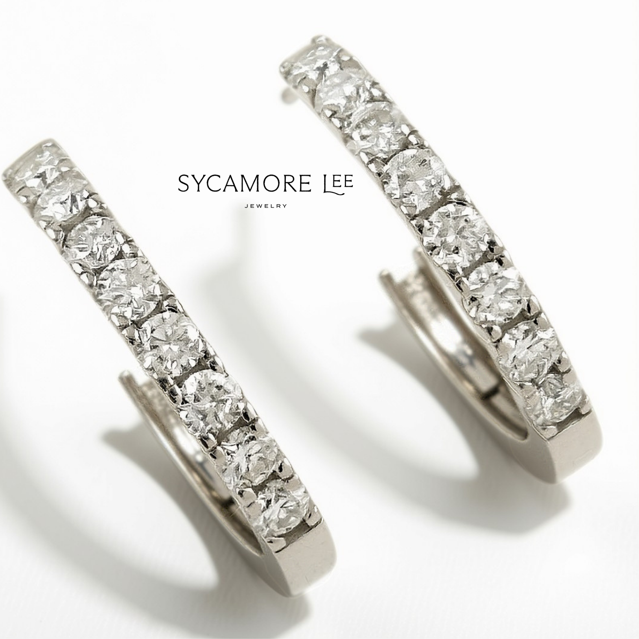 A pair of silver hoop earrings paved with clear round-cut gemstones, shown on a white background with the brand name 'SYCAMORE LEE JEWELRY' printed in the center.