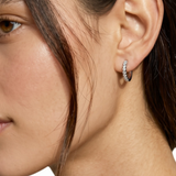 A close-up of a model's ear wearing a small silver hoop earring set with clear stones.