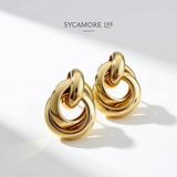 A pair of gold-toned chunky interlocking ring earrings by Sycamore Lee Jewelry, displayed on a clean white surface with soft diagonal shadows.