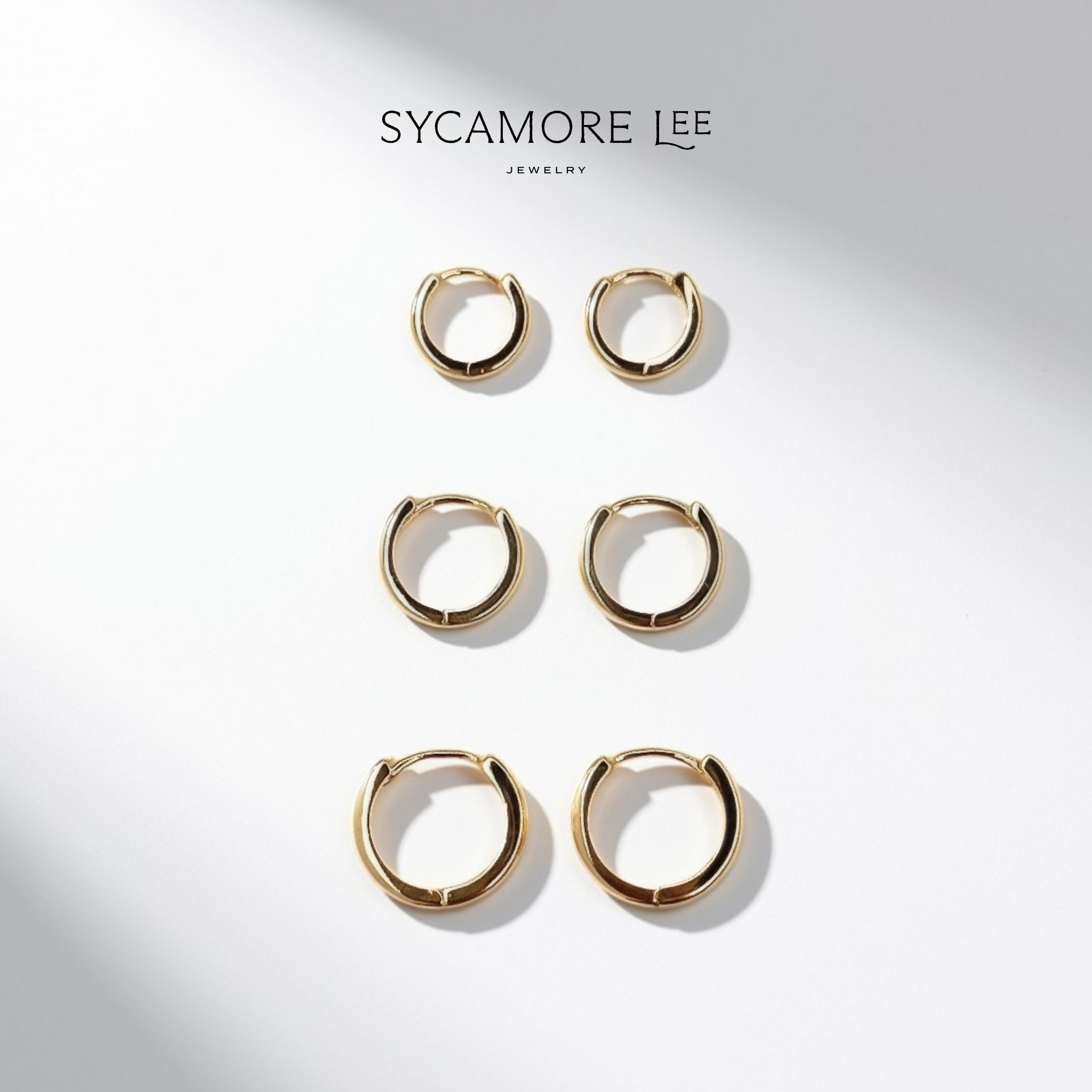 Six gold huggie hoop earrings arranged in two columns on a white background with soft diagonal shadows. The brand name 'SYCAMORE LEE JEWELRY' is printed at the top.