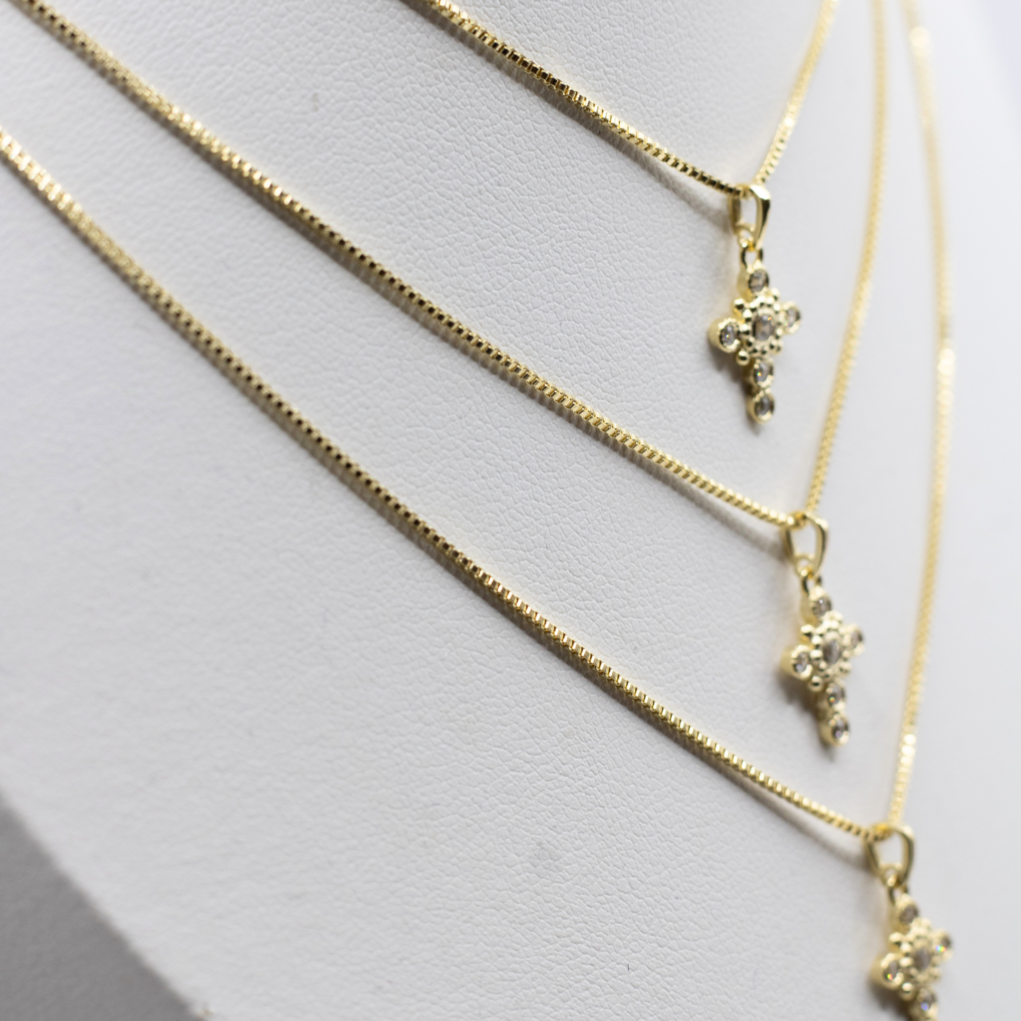 Three delicate gold chain necklaces with small floral or clover-like pendant charms, displayed on a white jewelry bust.