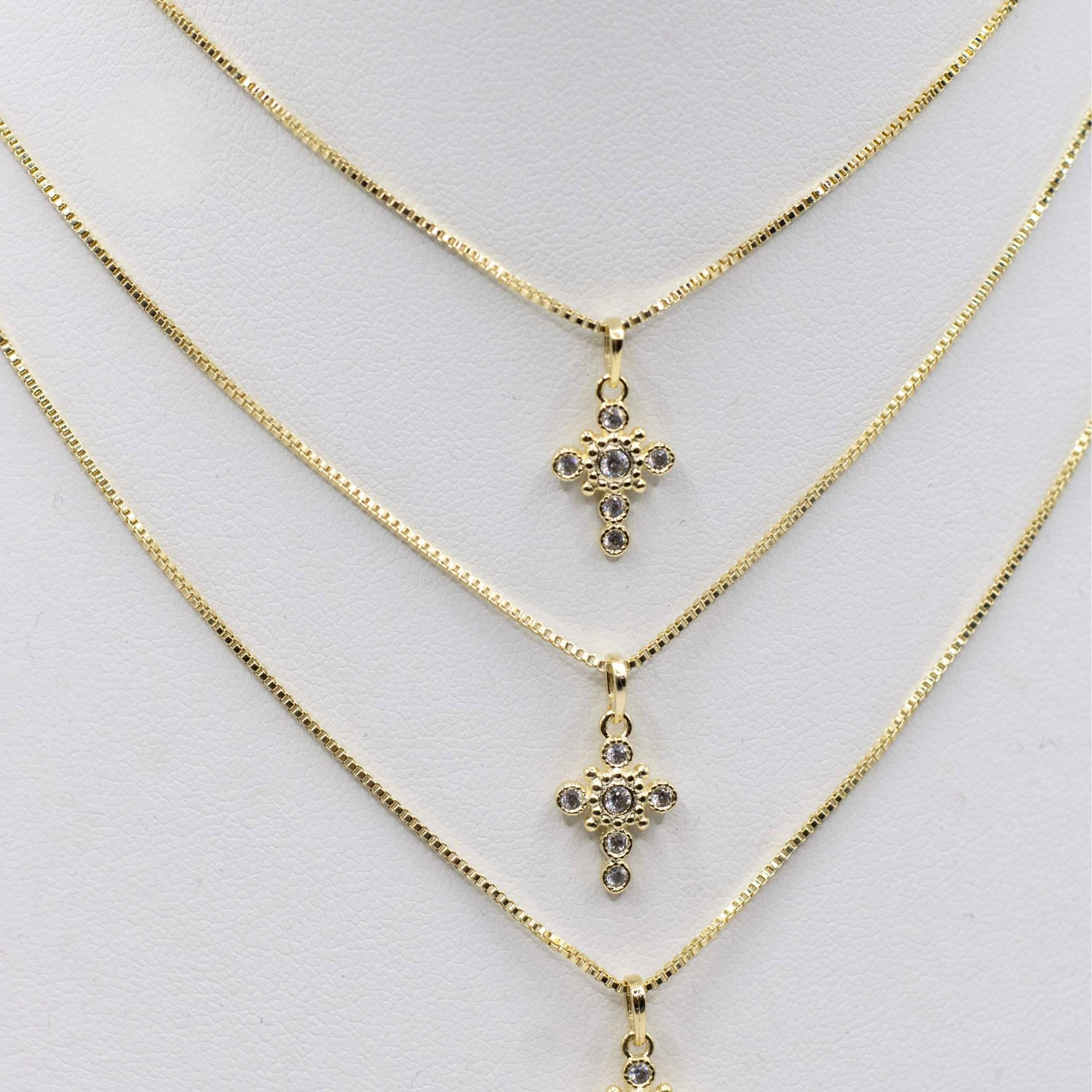 Three gold chain necklaces with matching cross pendants adorned with small clear rhinestones, displayed on a white jewelry bust.