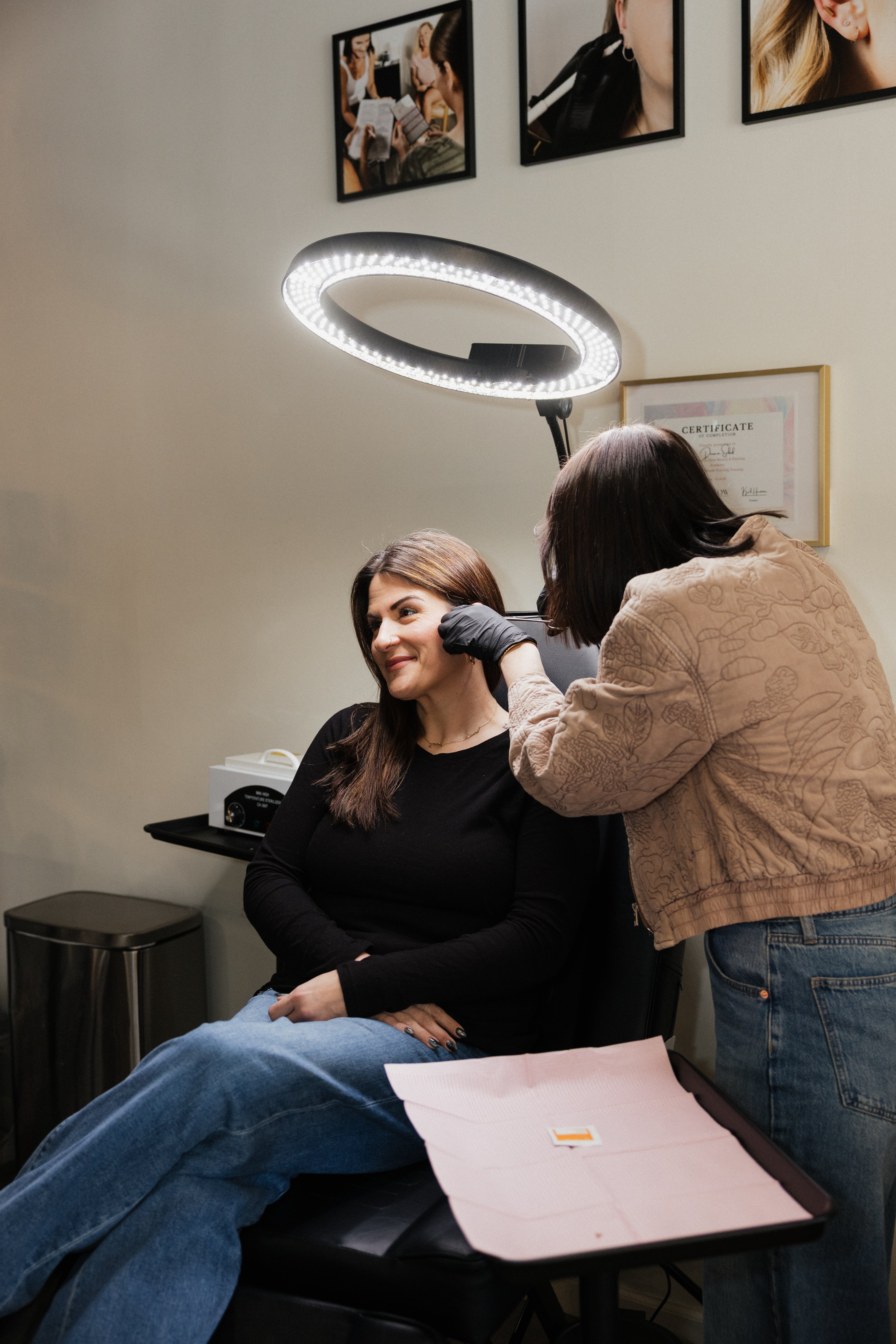 Woman getting a tattoo in a salon with a tattoo artist and a round LED lamp.