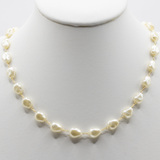 A delicate gold chain necklace featuring irregular, baroque-style cream-colored freshwater pearls, displayed on a white jewelry bust.