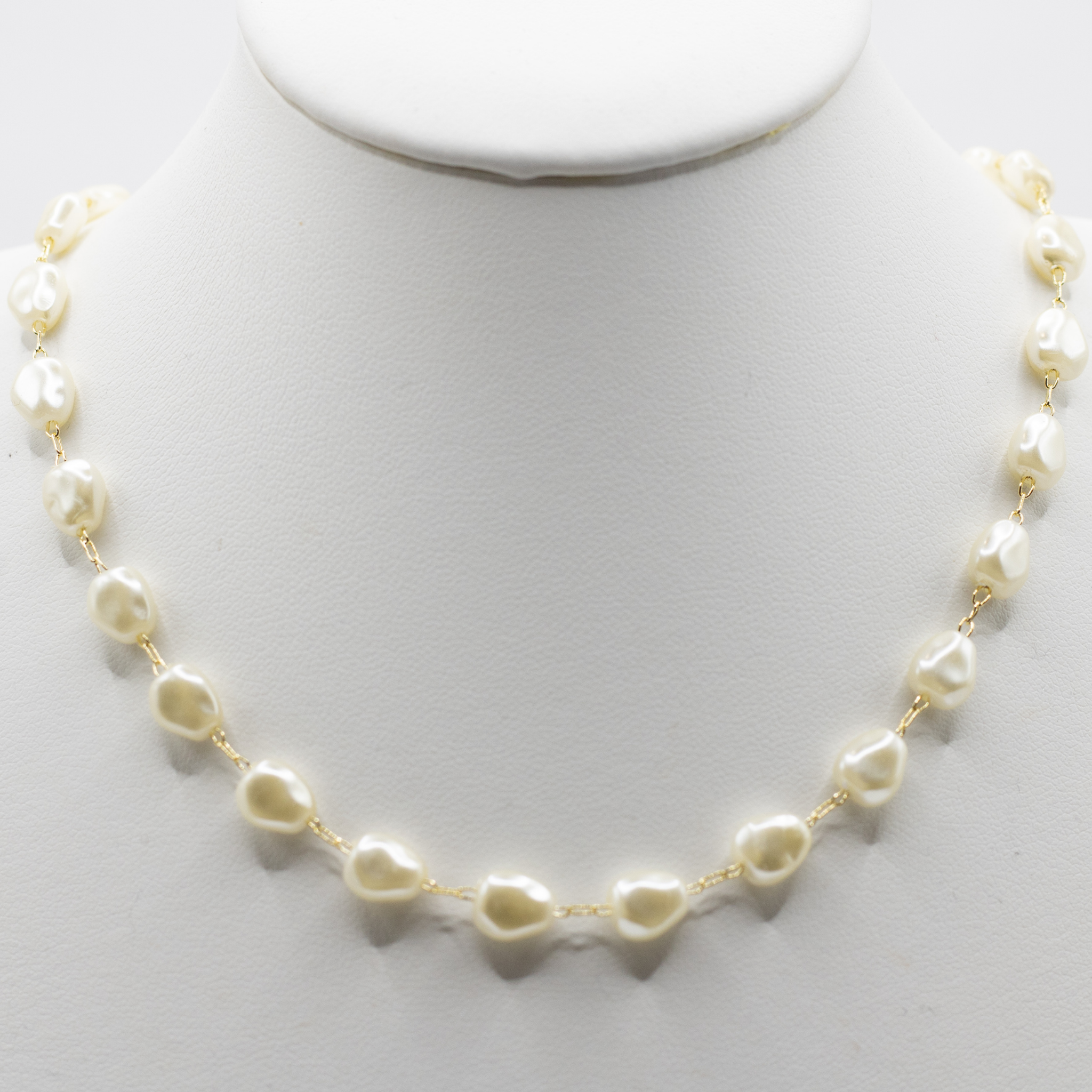 A delicate gold chain necklace featuring irregular, baroque-style cream-colored freshwater pearls, displayed on a white jewelry bust.