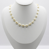 A delicate necklace made of small irregular cream-colored pearls on a gold chain, displayed on a white jewelry bust against a light gray background.