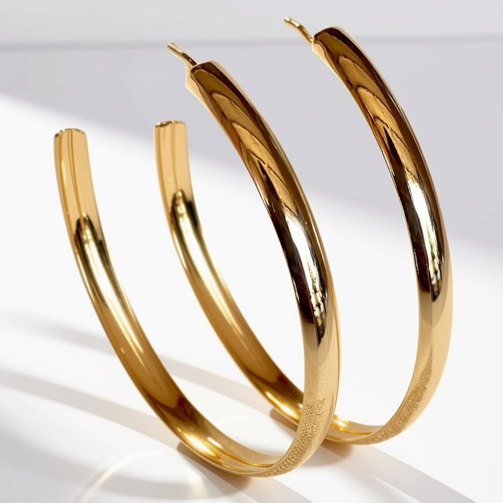 A pair of polished gold hoop earrings with a sleek, tapered design, displayed on a clean white surface with soft shadows.