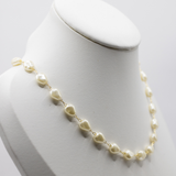 A delicate gold chain necklace featuring irregular cream-colored freshwater pearls, displayed on a white jewelry bust against a light gray background.