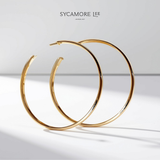 A pair of gold hoop earrings with a polished finish, displayed on a clean white background with a soft shadow. The brand name 'SYCAMORE LEE' is printed at the top center.