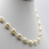 A close-up of a necklace with irregular cream-colored pearls connected by small gold chains, displayed on a white mannequin bust.