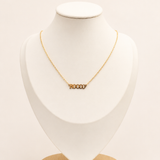 Gold necklace on a white bust with a wooden base against a beige background