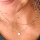A close-up lifestyle shot of a woman wearing a delicate double-layered silver necklace with a small miraculous medal pendant on a sterling silver delicate cable chain. 