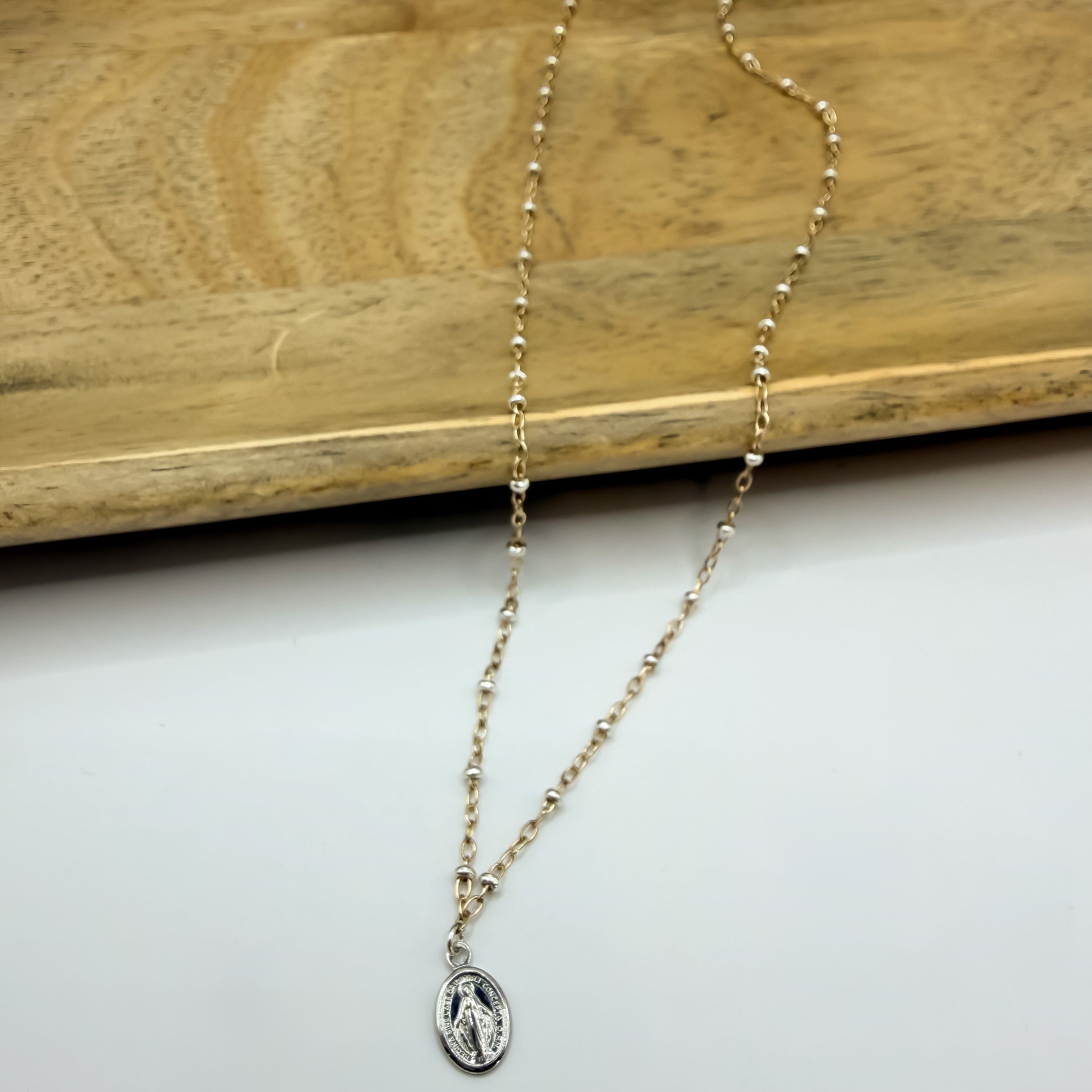 A delicate mixed metal chain necklace with a small oval Saint Benedict miraculous medal pendant.