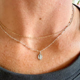 A close-up lifestyle shot of a woman wearing a delicate double-layered silver necklace with a small miraculous medal pendant on a sterling silver delicate cable chain. 